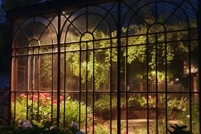 Miniature Location salle Verderonne (Oise) - Domaine de Verderonne #28 Serre illuminée au crépuscule, entourée de murs en pierre et d'arbres, avec une tour en arrière-plan.