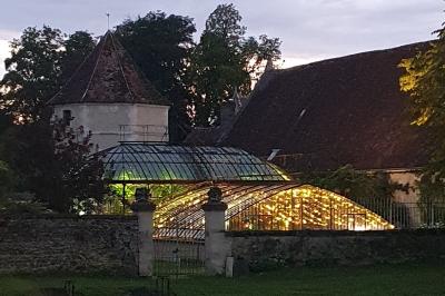 Miniature Location salle Verderonne (Oise) - Domaine de Verderonne #36 Serre illuminée au crépuscule, entourée de murs en pierre et d'arbres, avec une tour en arrière-plan.