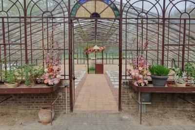 Miniature Location salle Verderonne (Oise) - Domaine de Verderonne #15 Serre illuminée au crépuscule, entourée de murs en pierre et d'arbres, avec une tour en arrière-plan.