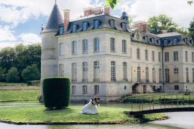 Miniature Location salle Verderonne (Oise) - Domaine de Verderonne #11 Un couple en tenue de mariage marche dans un jardin verdoyant sous une lumière naturelle.