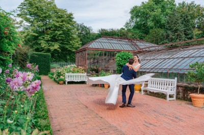Miniature Location salle Verderonne (Oise) - Domaine de Verderonne #15 Un couple en tenue de mariage marche dans un jardin verdoyant sous une lumière naturelle.