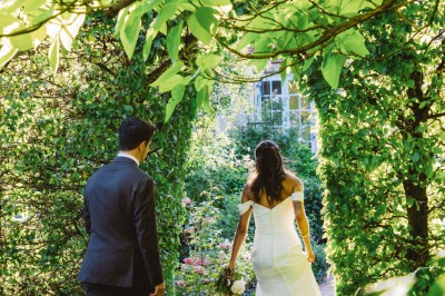 Miniature Location salle Verderonne (Oise) - Domaine de Verderonne #16 Un couple en tenue de mariage marche dans un jardin verdoyant sous une lumière naturelle.