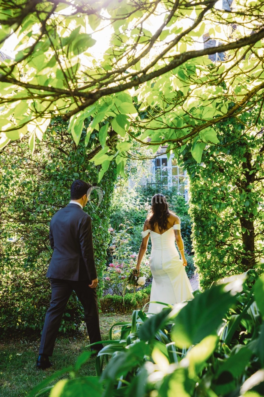 Un couple en tenue de mariage marche dans un jardin verdoyant sous une lumière naturelle.