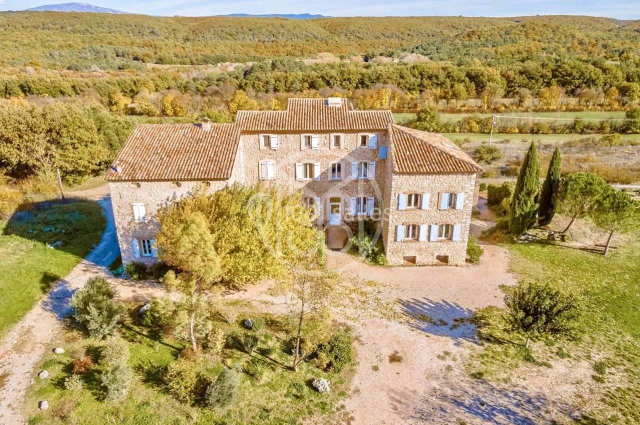 Vue aérienne d'une grande maison en pierre entourée de végétation, située dans un paysage rural.
