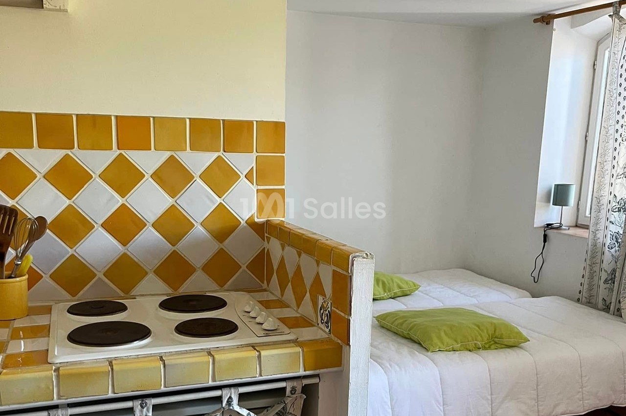 Cuisine avec plaques de cuisson et crédence en carreaux jaunes, attenante à une chambre avec lit et coussins verts.
