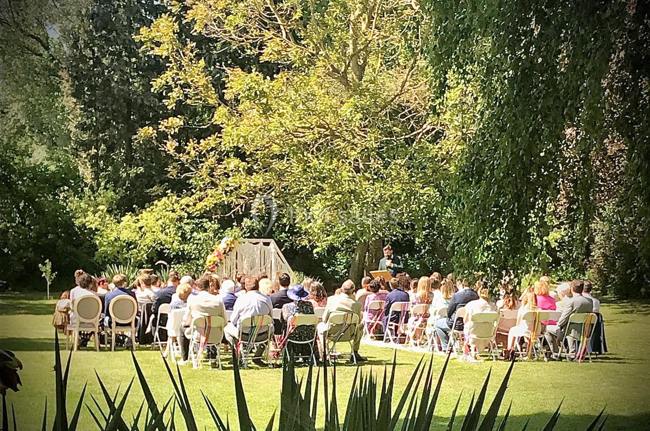 Cérémonie en plein air avec des invités assis devant un officiant, dans un jardin verdoyant et ensoleillé.