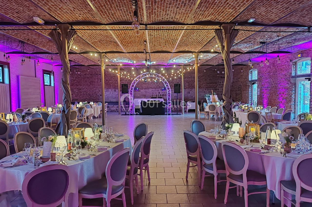 Salle de réception décorée avec des tables dressées, éclairage tamisé et guirlandes lumineuses suspendues.
