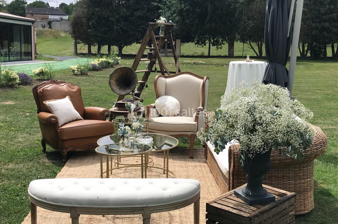 Mobilier vintage disposé en extérieur avec fauteuils, table basse, gramophone et décoration florale sur pelouse.