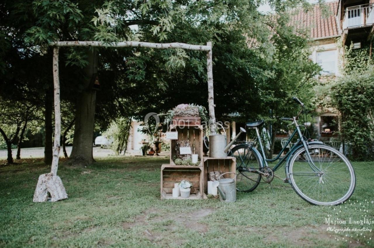 Un vélo ancien posé près de caisses en bois et d'objets décoratifs dans un jardin verdoyant.