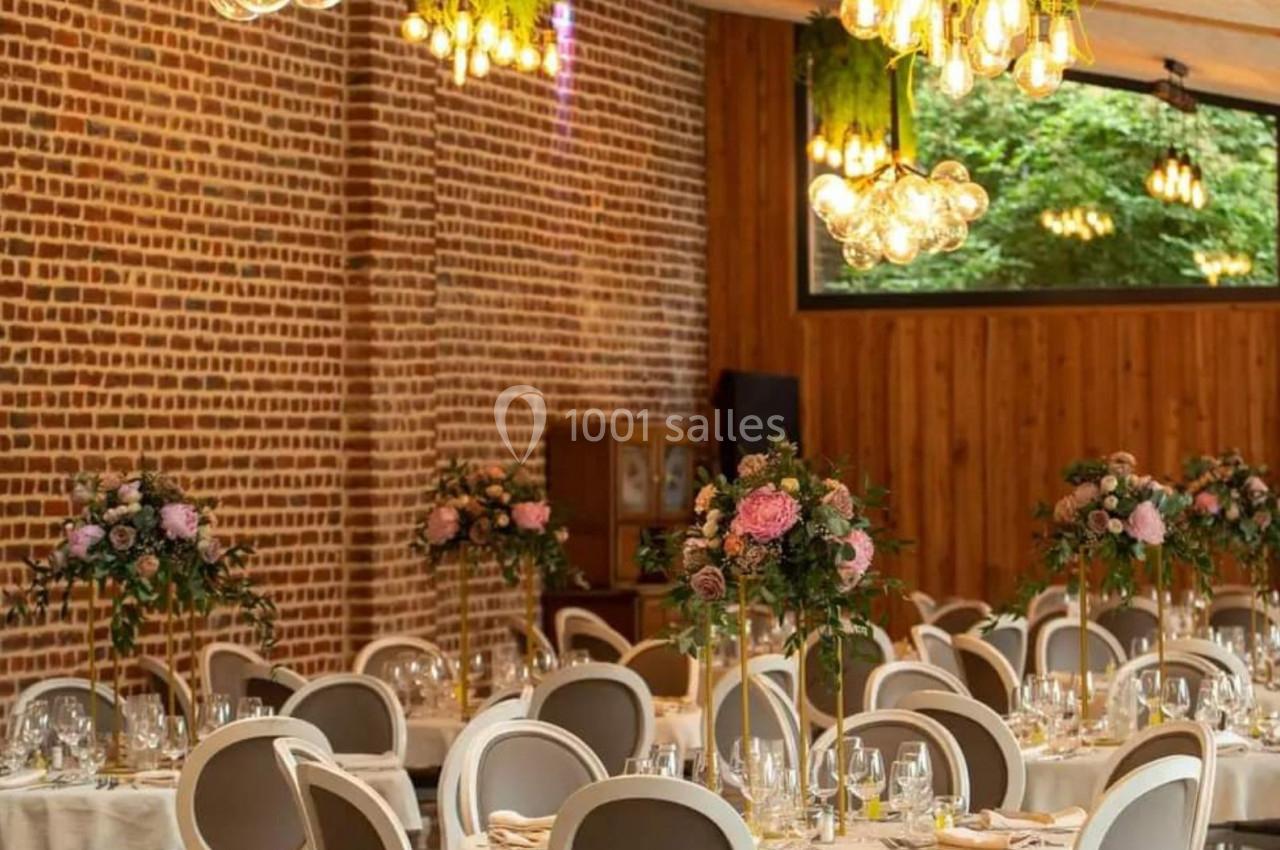 Salle de réception élégante avec murs en briques, tables rondes décorées de fleurs et luminaires suspendus.