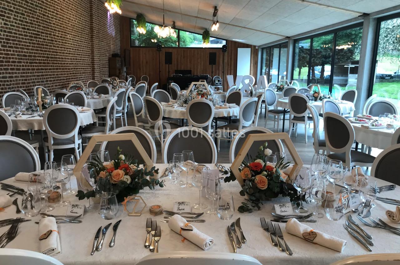 Salle de réception décorée avec des tables dressées, ornées de bouquets de fleurs et de vaisselle élégante.