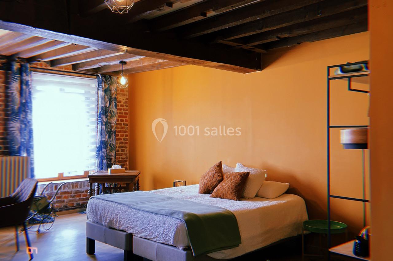 Chambre avec lit double, poutres apparentes, mur orange, bureau près d'une fenêtre et décoration minimaliste.