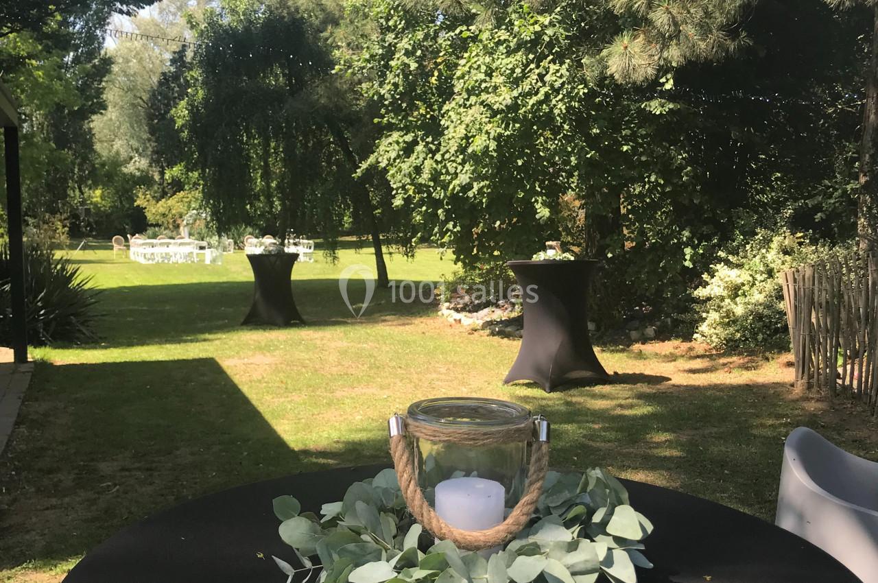 Table haute noire décorée de feuilles et d'une bougie dans un jardin verdoyant avec des tables en arrière-plan.