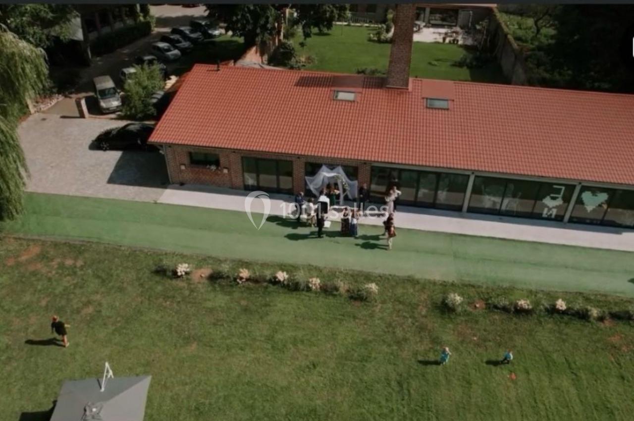 Vue aérienne d'un bâtiment avec toit rouge, entouré de pelouse, où un groupe de personnes est rassemblé à l'entrée.