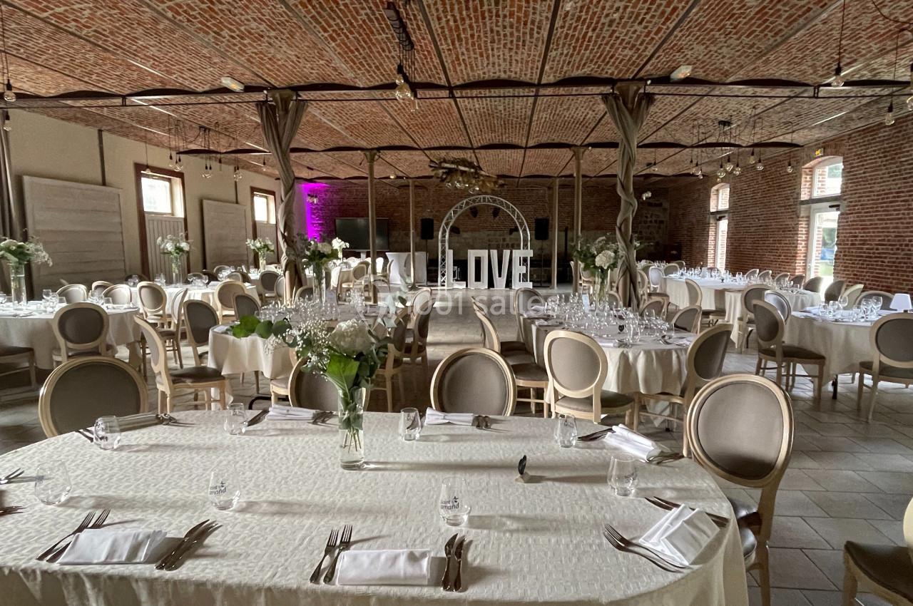 Salle de réception avec tables rondes dressées, décorations florales et arche lumineuse inscrite ’LOVE’.