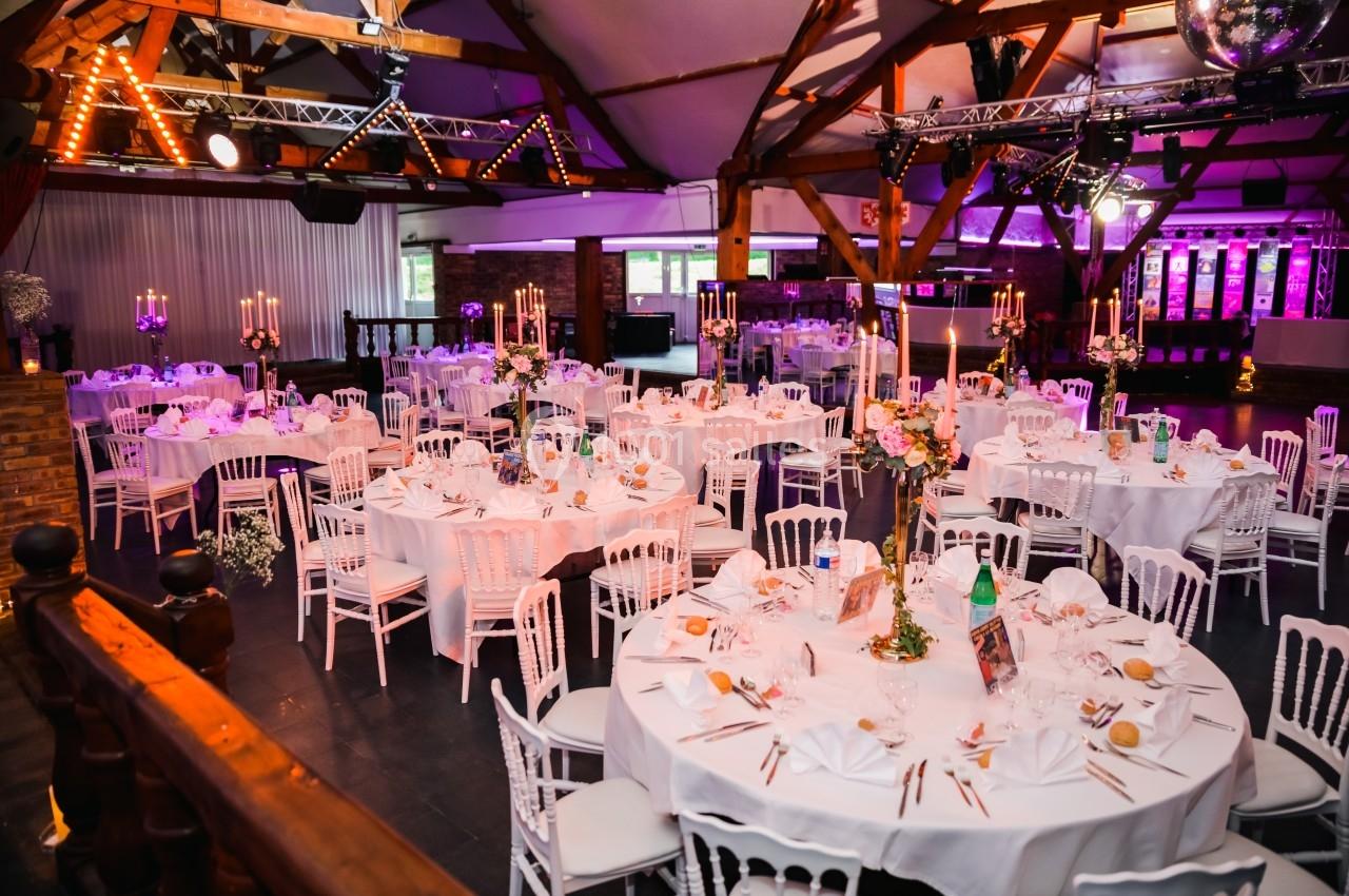 Salle de réception décorée avec des tables rondes dressées, chandeliers et éclairage tamisé dans une ambiance festive.