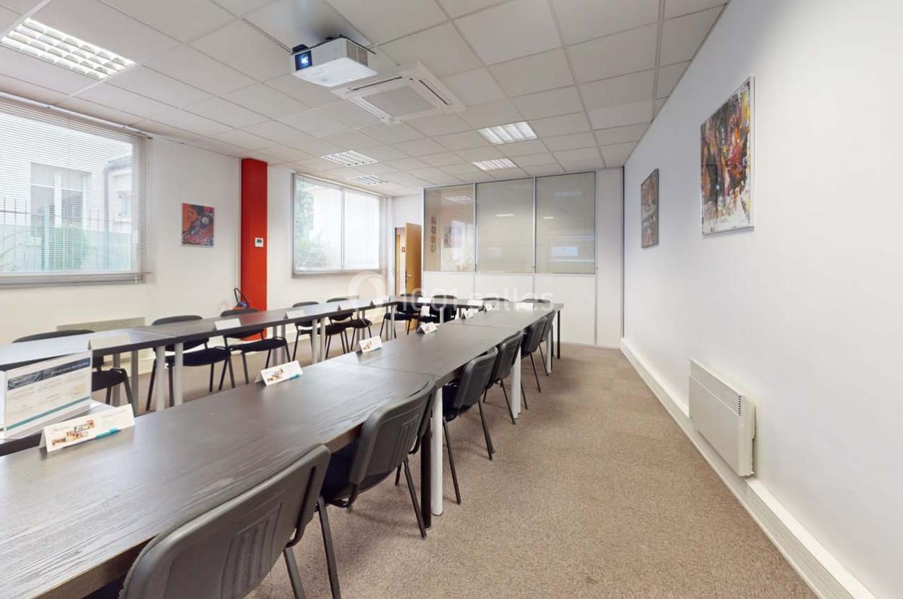 Salle de réunion lumineuse avec tables en U, chaises noires, tableaux aux murs et équipement de projection au plafond.