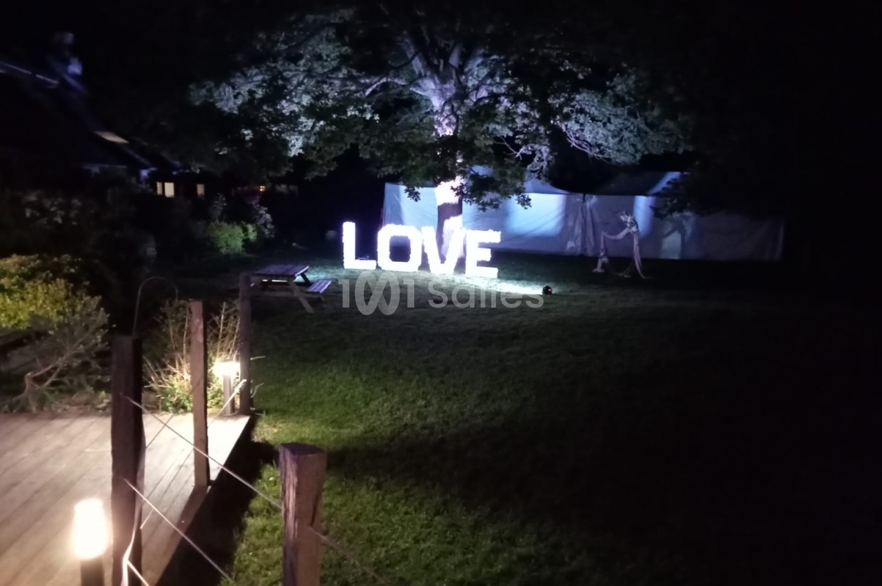 Lettres lumineuses formant le mot ’LOVE’ installées sur une pelouse, éclairées dans un jardin sombre.