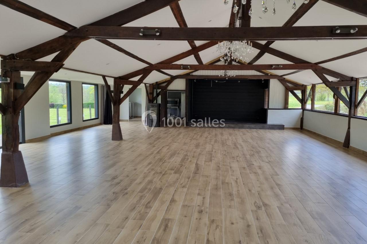Salle spacieuse avec charpente en bois apparente, parquet clair, scène noire et grandes baies vitrées donnant sur l…