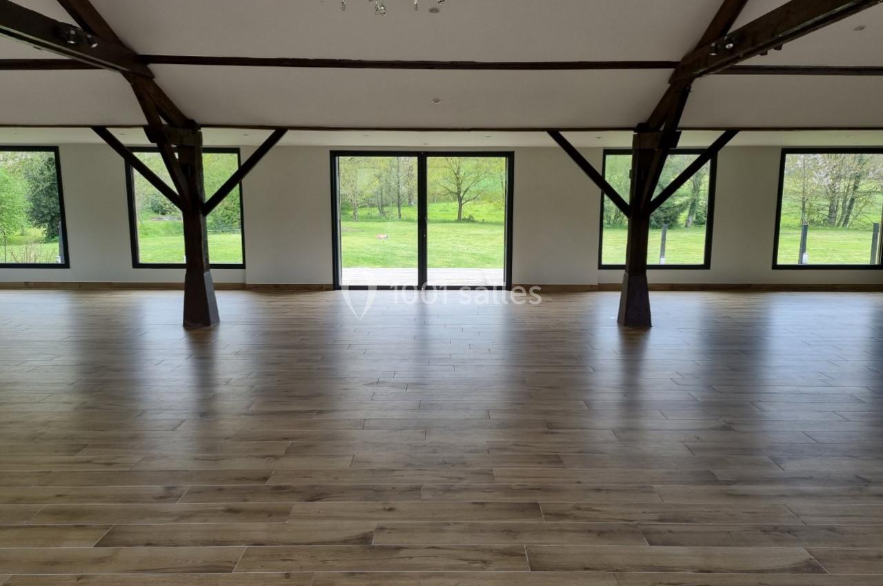 Salle lumineuse avec parquet en bois, poutres apparentes et grandes baies vitrées donnant sur un jardin verdoyant.