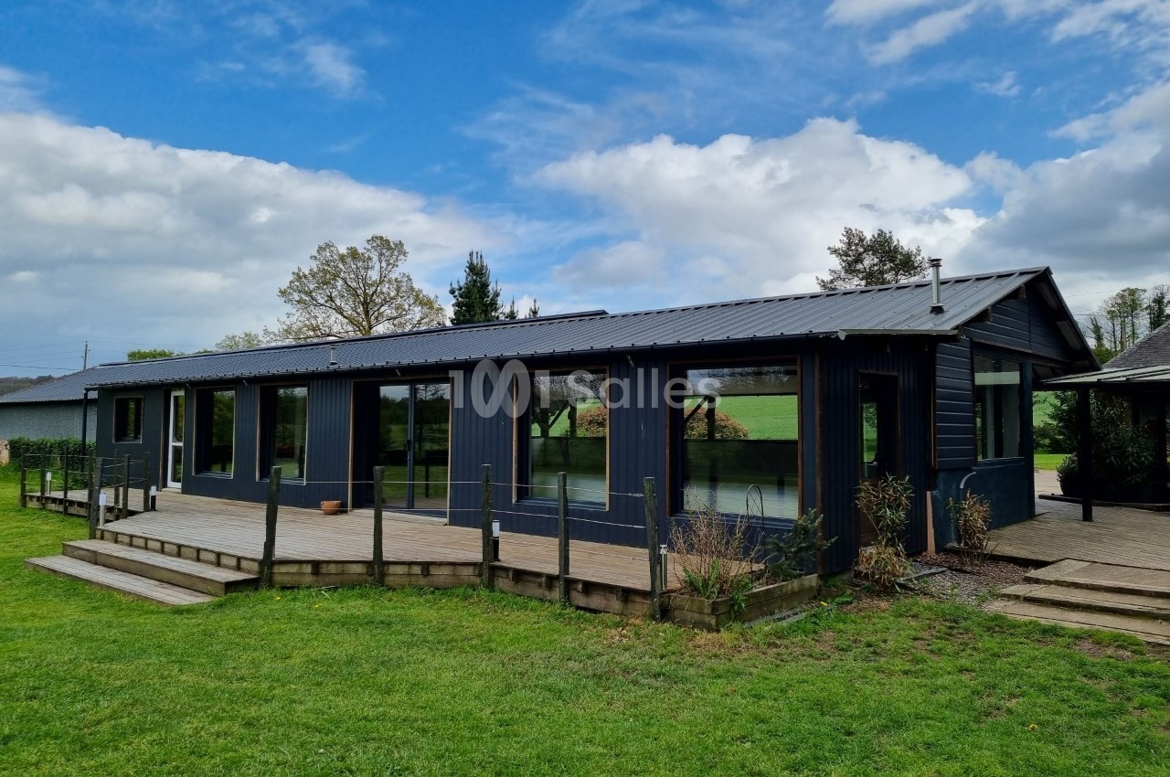 Maison moderne de plain-pied avec bardage sombre, grandes baies vitrées et terrasse en bois, entourée de verdure.