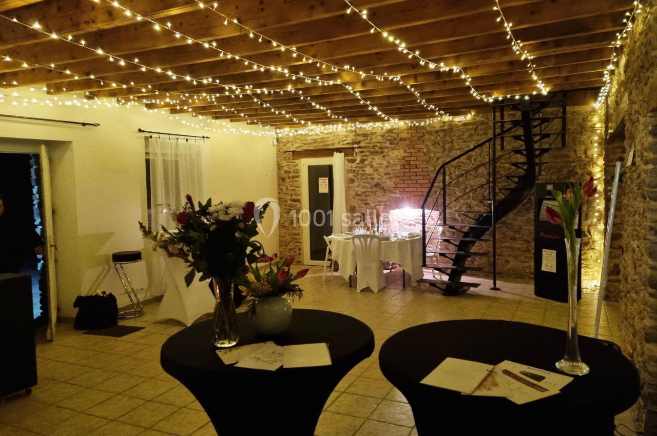 Salle décorée avec des guirlandes lumineuses, tables dressées et fleurs, avec un escalier en colimaçon en arrière-plan.