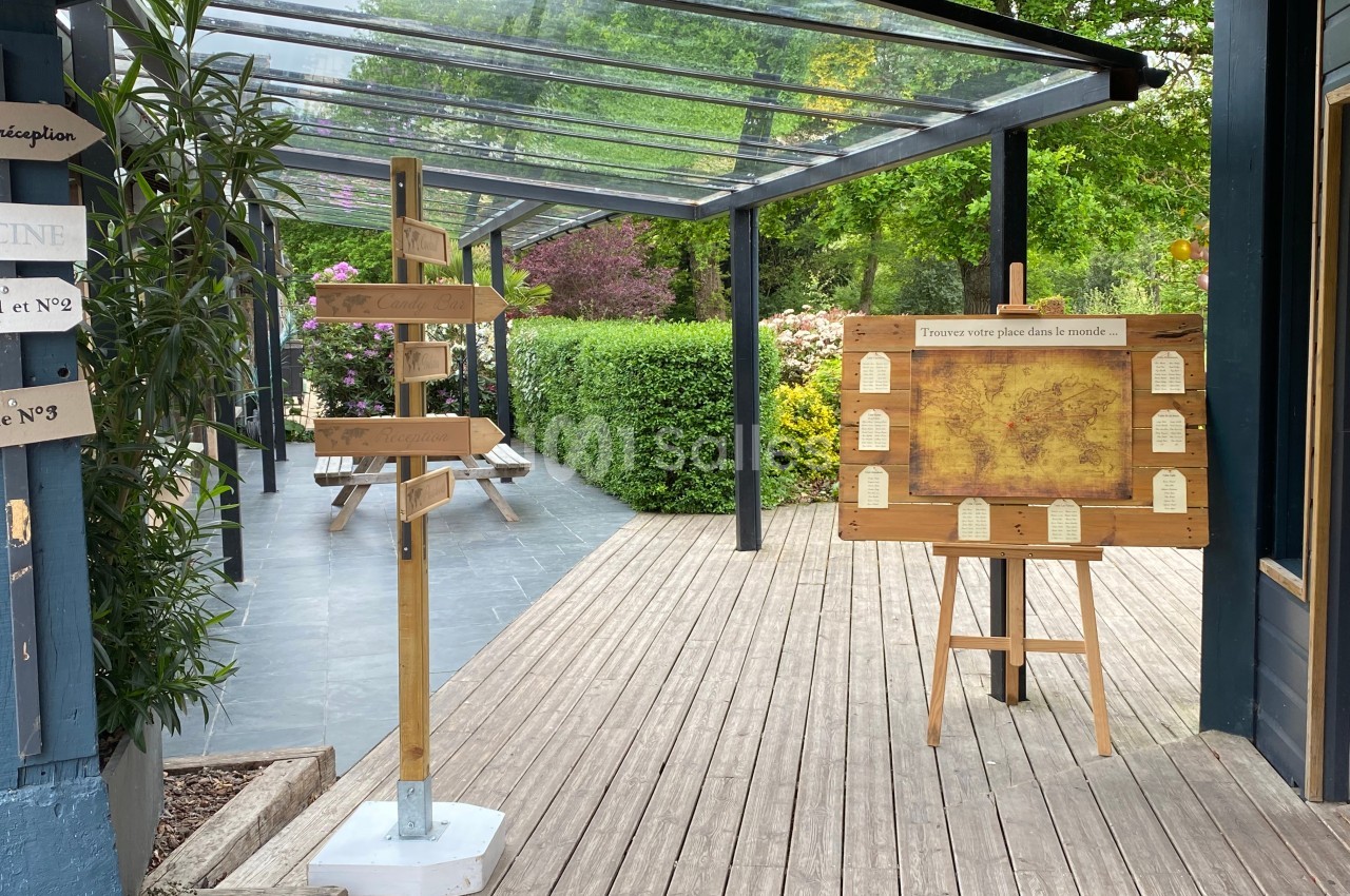 Panneau directionnel en bois et tableau d'affichage sur une terrasse en bois entourée de végétation.