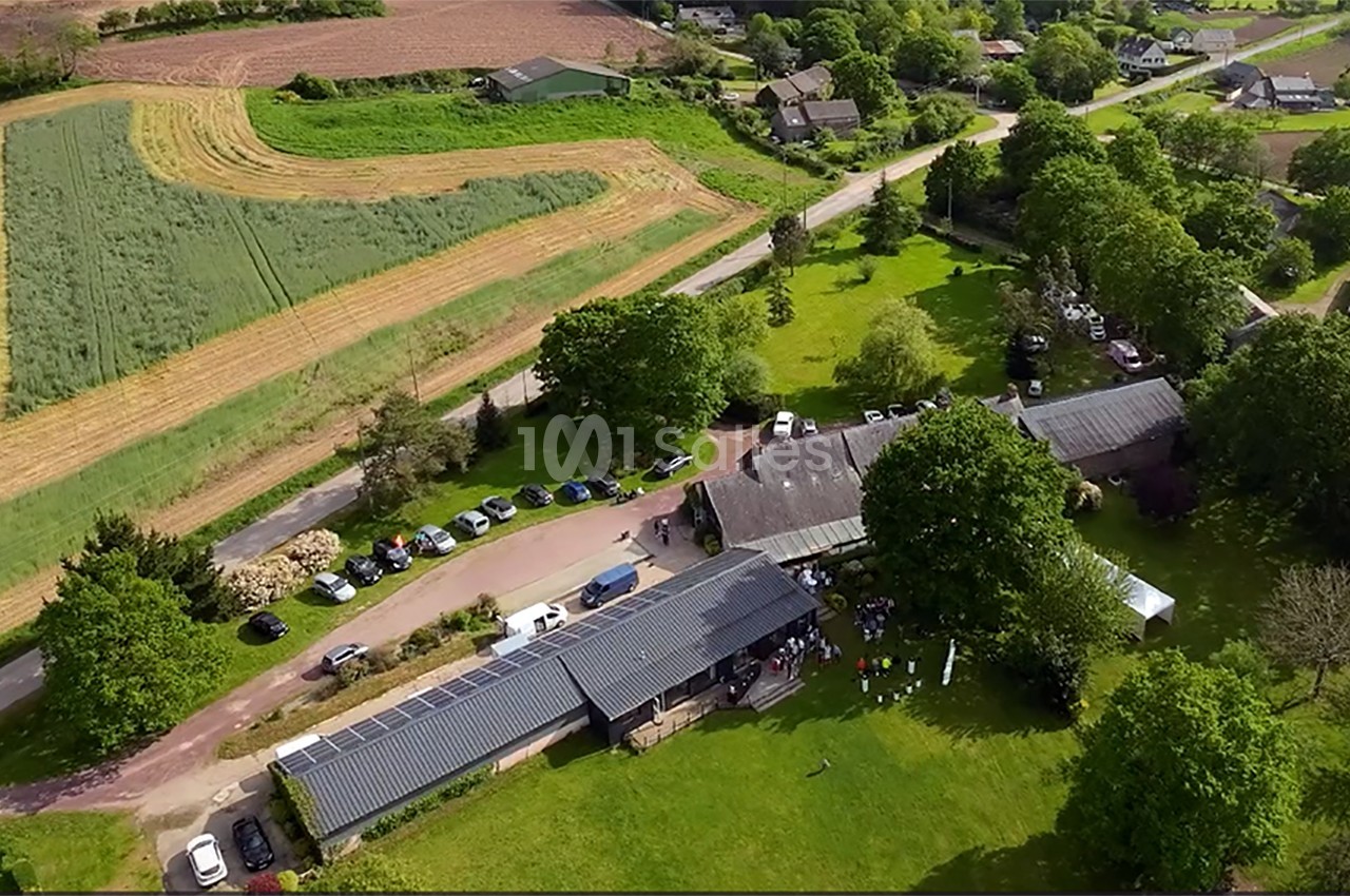 Vue aérienne d'un complexe de bâtiments entouré de champs, d'arbres et de voitures stationnées le long d'une route.
