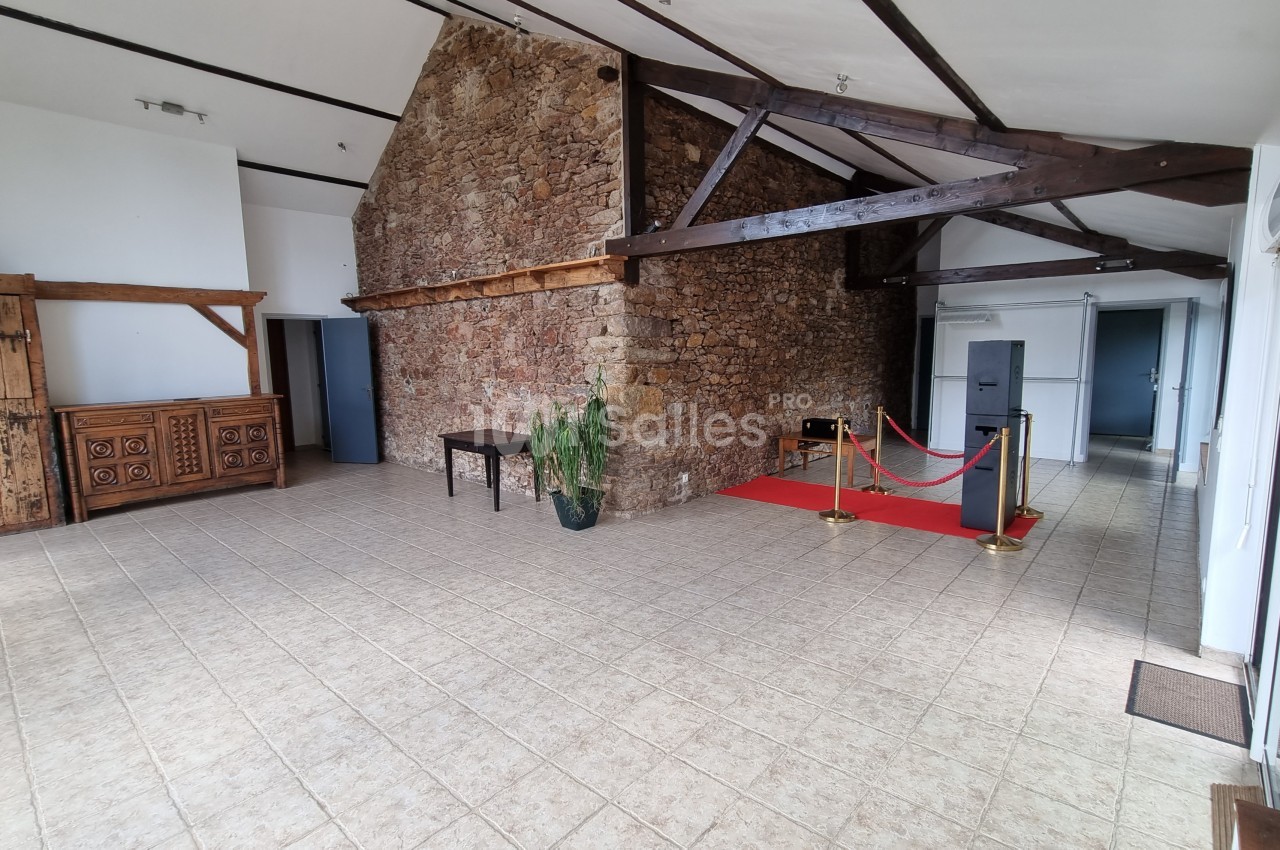 Salle lumineuse avec murs en pierre, poutres apparentes, carrelage beige, tapis rouge et mobilier en bois rustique.