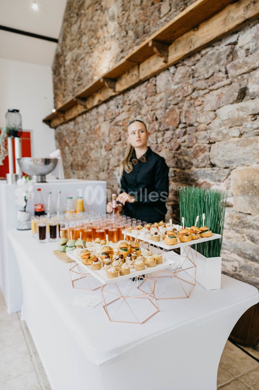 Serveuse derrière une table de buffet garnie de cocktails, amuse-bouches et décorations dans un cadre en pierre.