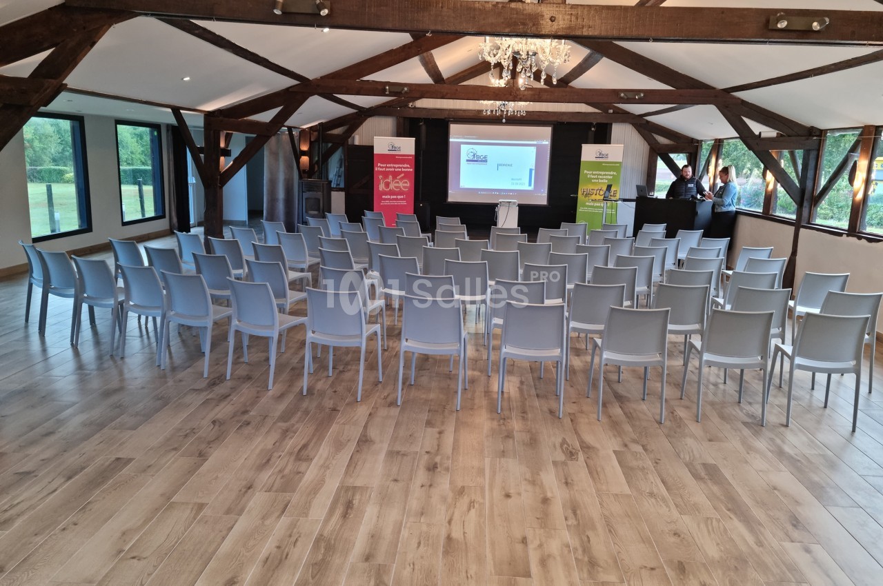 Salle de conférence avec des rangées de chaises vides, un écran de projection et des affiches promotionnelles.