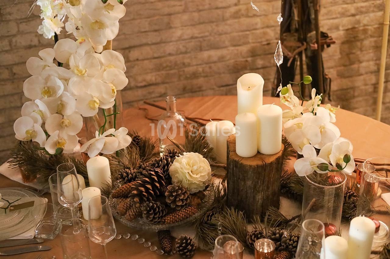 Table décorée avec des bougies blanches, des fleurs d'orchidées, des pommes de pin et des branches de sapin.