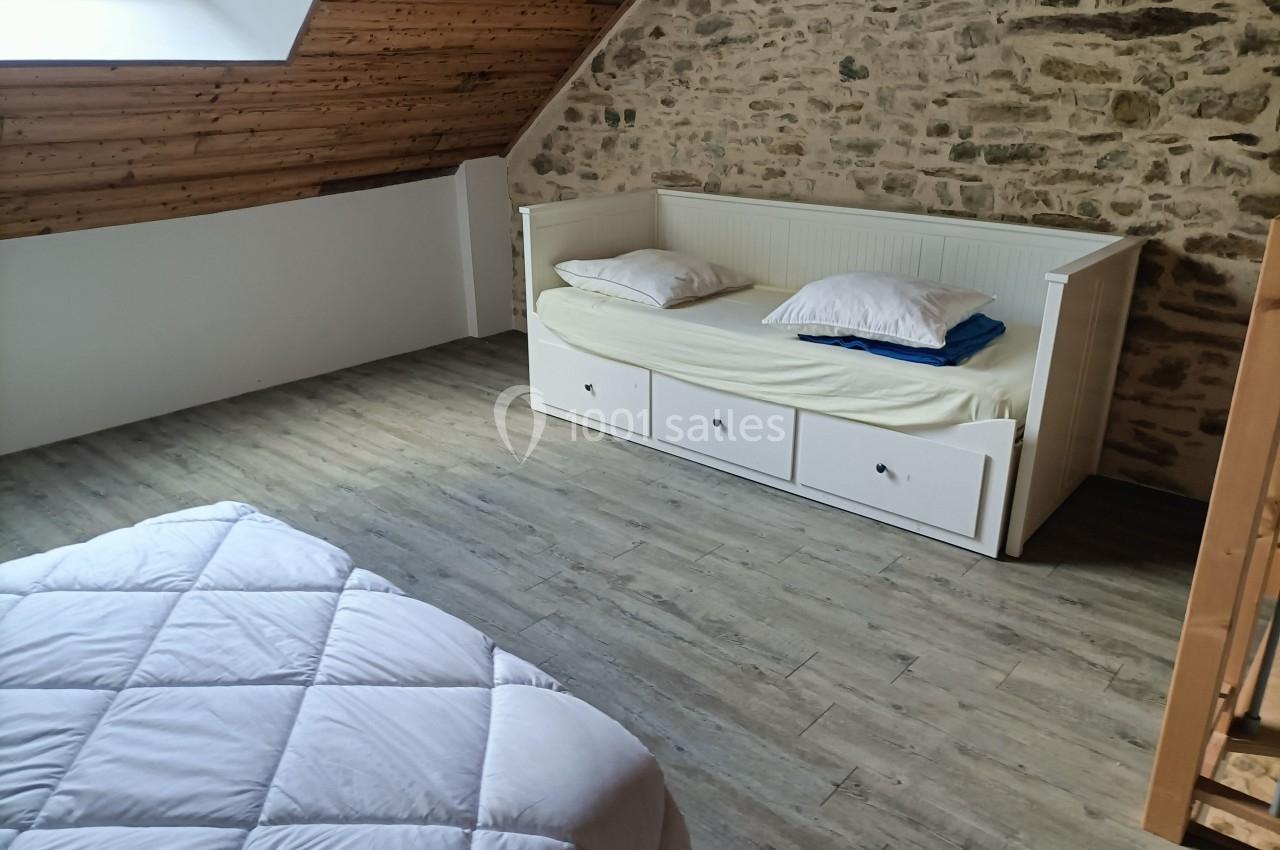 Lit gigogne blanc avec tiroirs dans une chambre mansardée, parquet en bois et mur en pierre apparente.