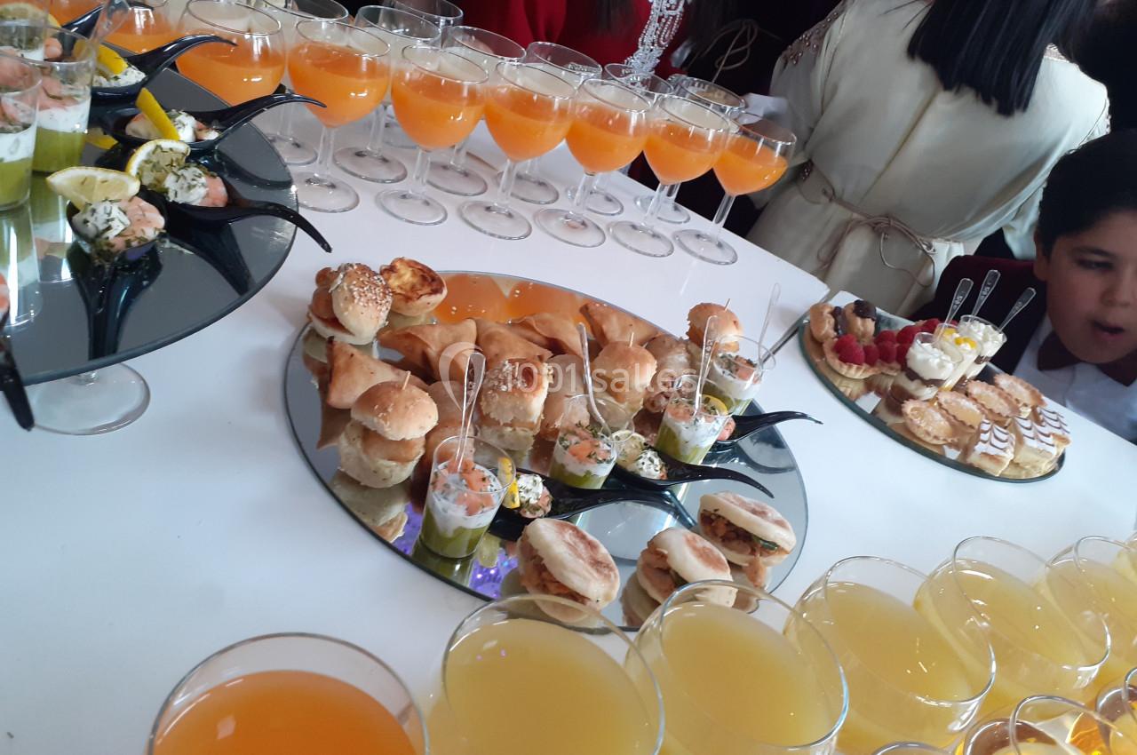 Buffet avec verrines, mini-sandwichs et jus de fruits sur une table blanche, entouré de convives.