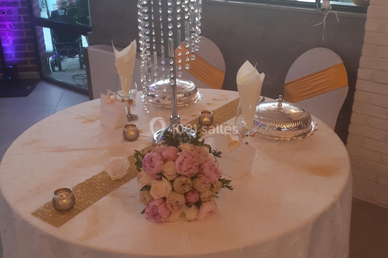 Table décorée pour un événement avec nappes blanches, centre de table floral, chandelles et éléments dorés.