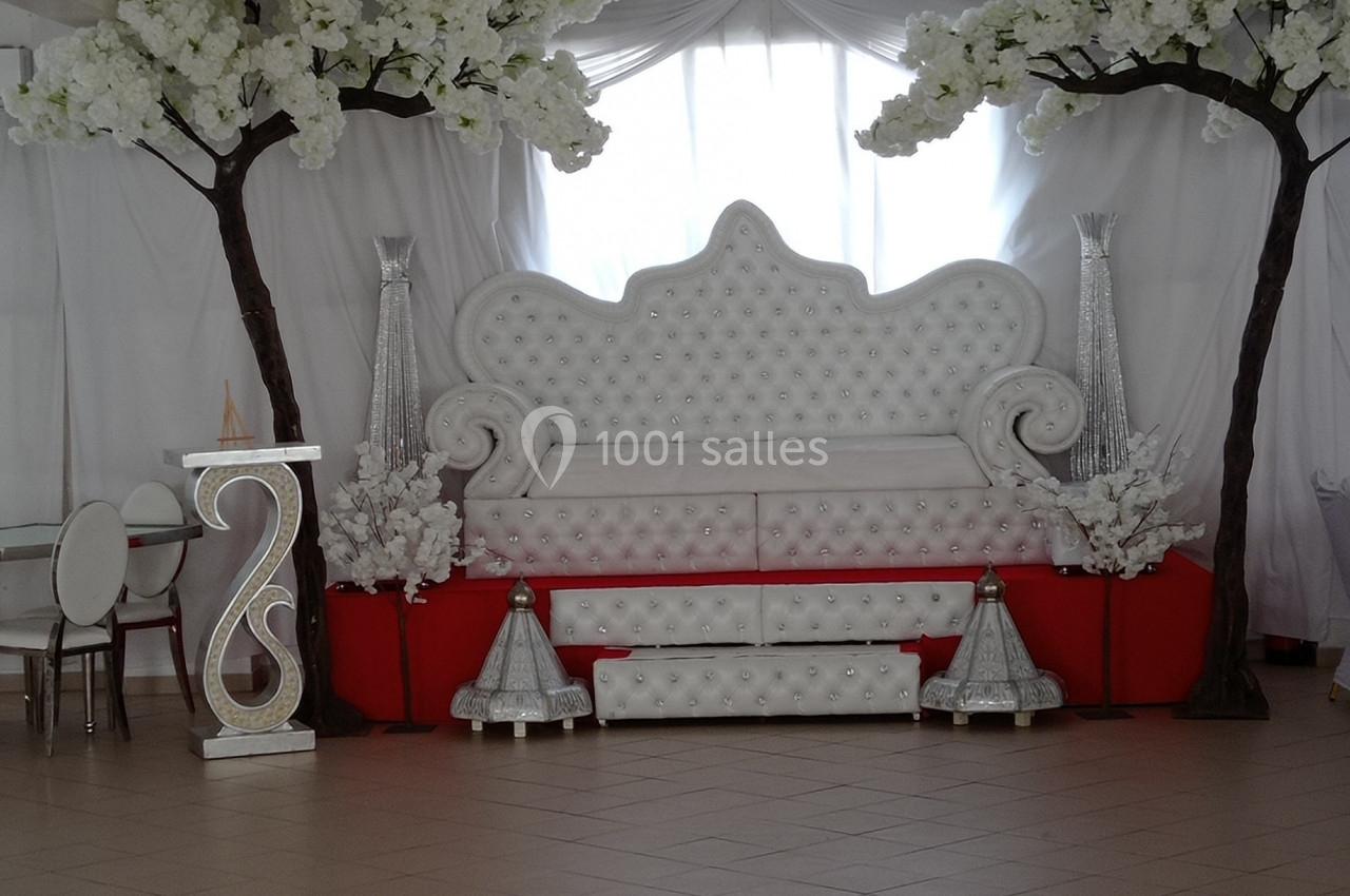 Salle décorée avec un canapé capitonné blanc, des arbres artificiels fleuris et des éléments décoratifs argentés.
