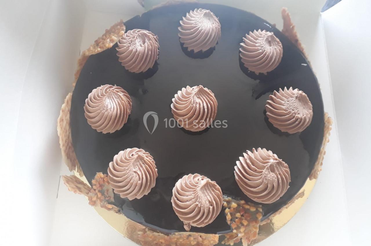 Gâteau rond avec glaçage chocolat brillant, décoré de huit rosaces de crème et de morceaux de nougatine sur les bords.