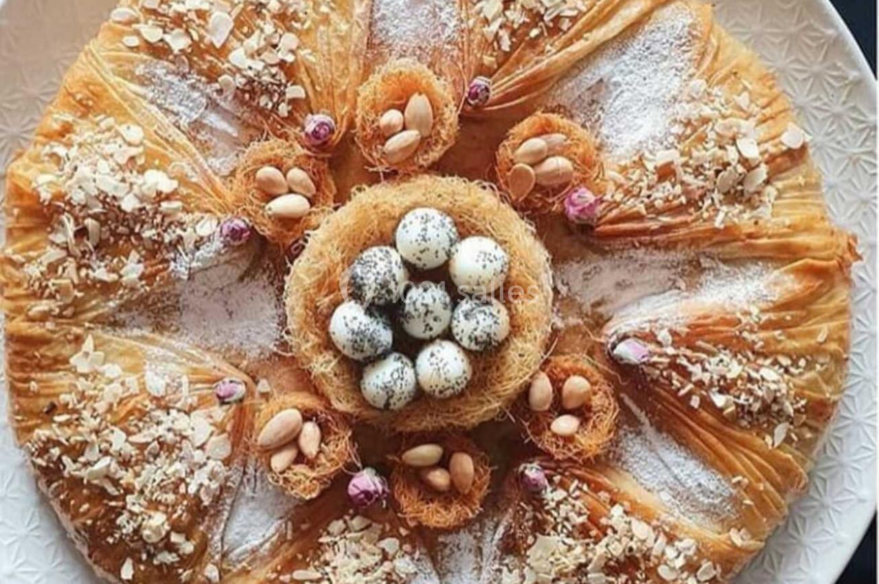 Pâtisserie circulaire en pâte filo garnie de fruits secs, sucre glace et œufs décoratifs au centre.
