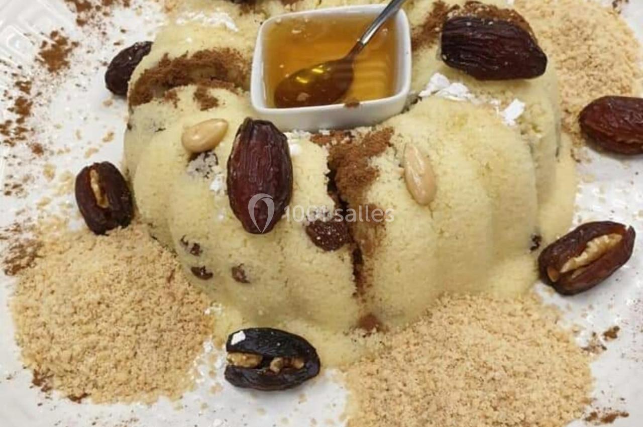 Assiette de semoule garnie de dattes, amandes, cannelle, miel au centre et poudre de biscuit autour.