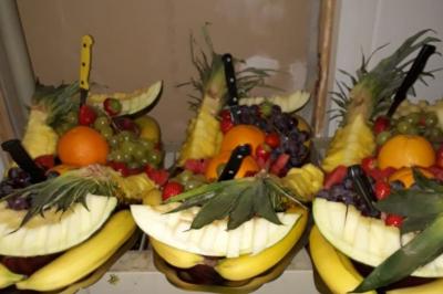 Plateaux de fruits frais composés de bananes, ananas, raisins, fraises, oranges et pastèques, décorés avec des couteaux.