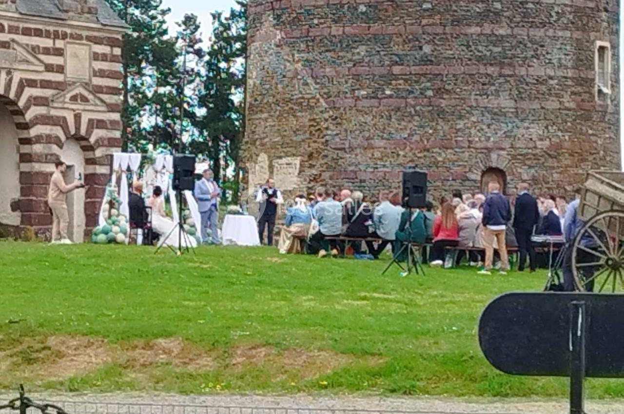 Cérémonie en plein air avec des invités assis près d'une tour en pierre et d'une arche décorée.