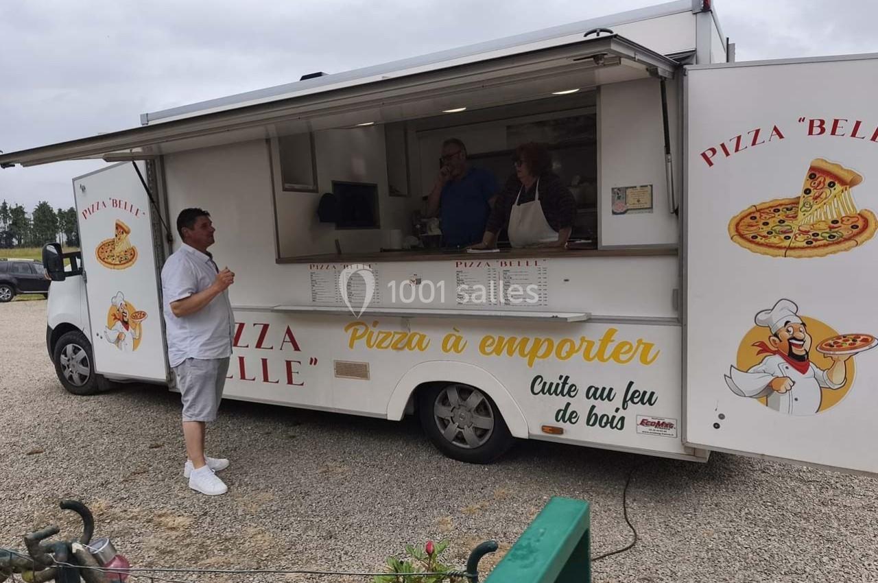 Camion de pizza à emporter avec menu affiché, un client discute avec le personnel à l'intérieur.