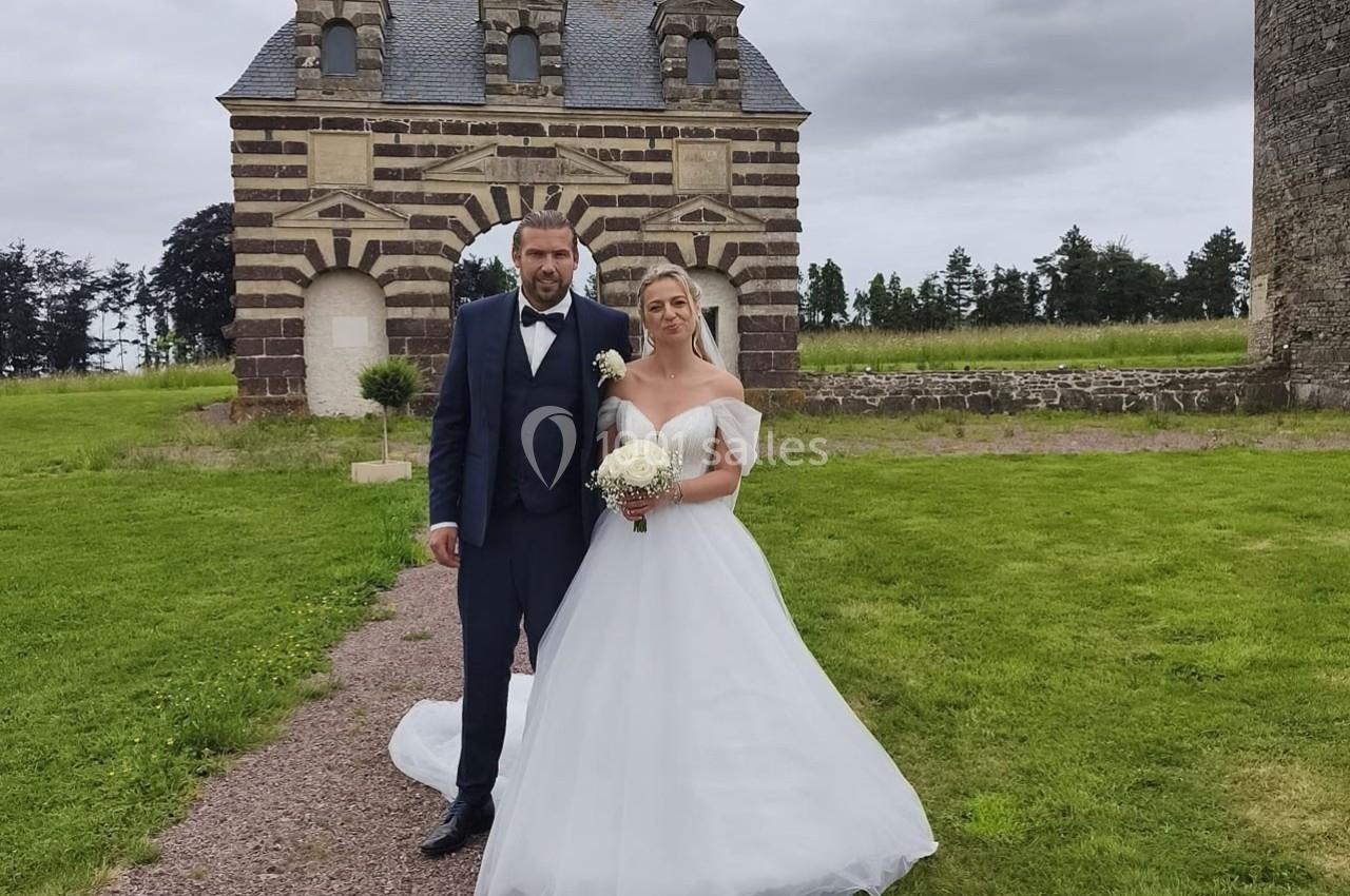 Un couple en tenue de mariage pose devant une arche en pierre dans un cadre verdoyant.