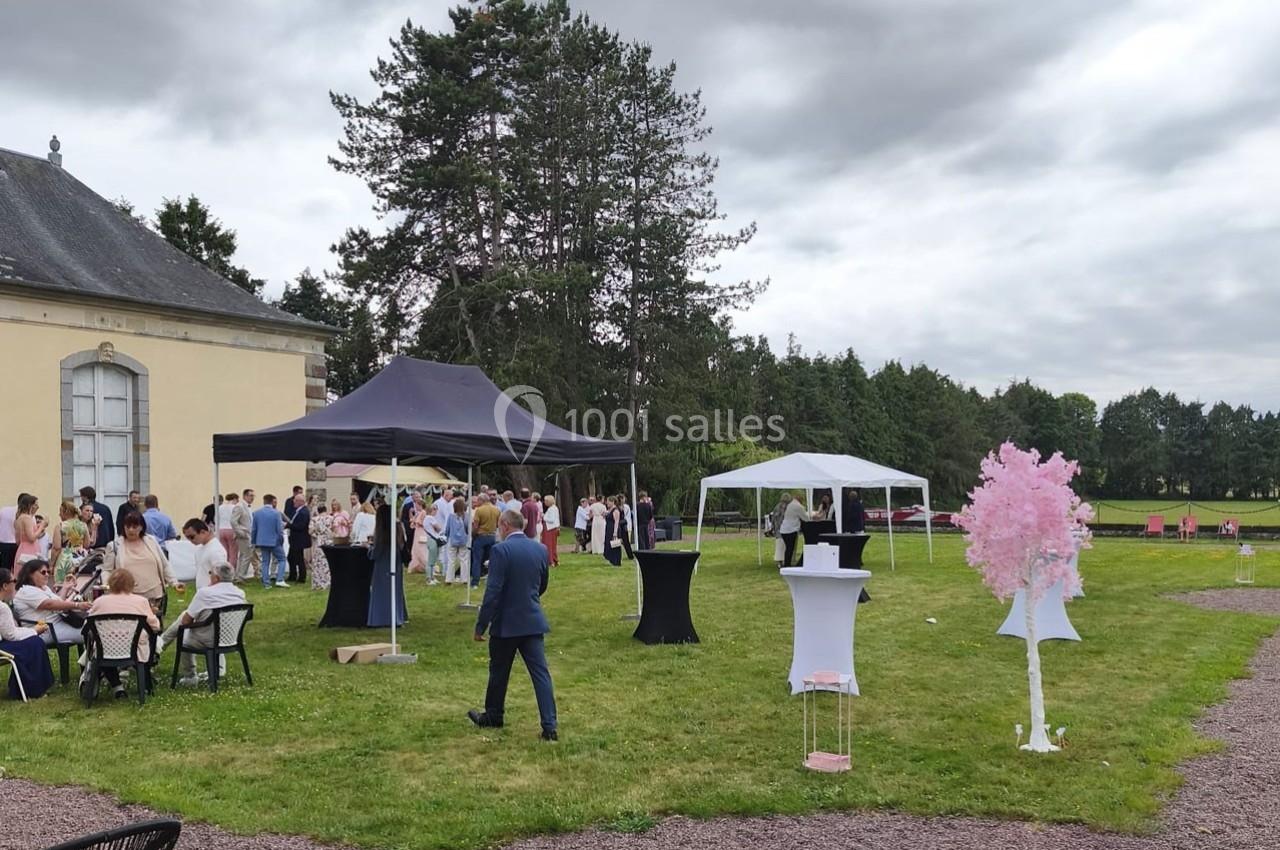 Personnes rassemblées dans un jardin pour un événement, avec tentes, tables et décorations sous un ciel nuageux.