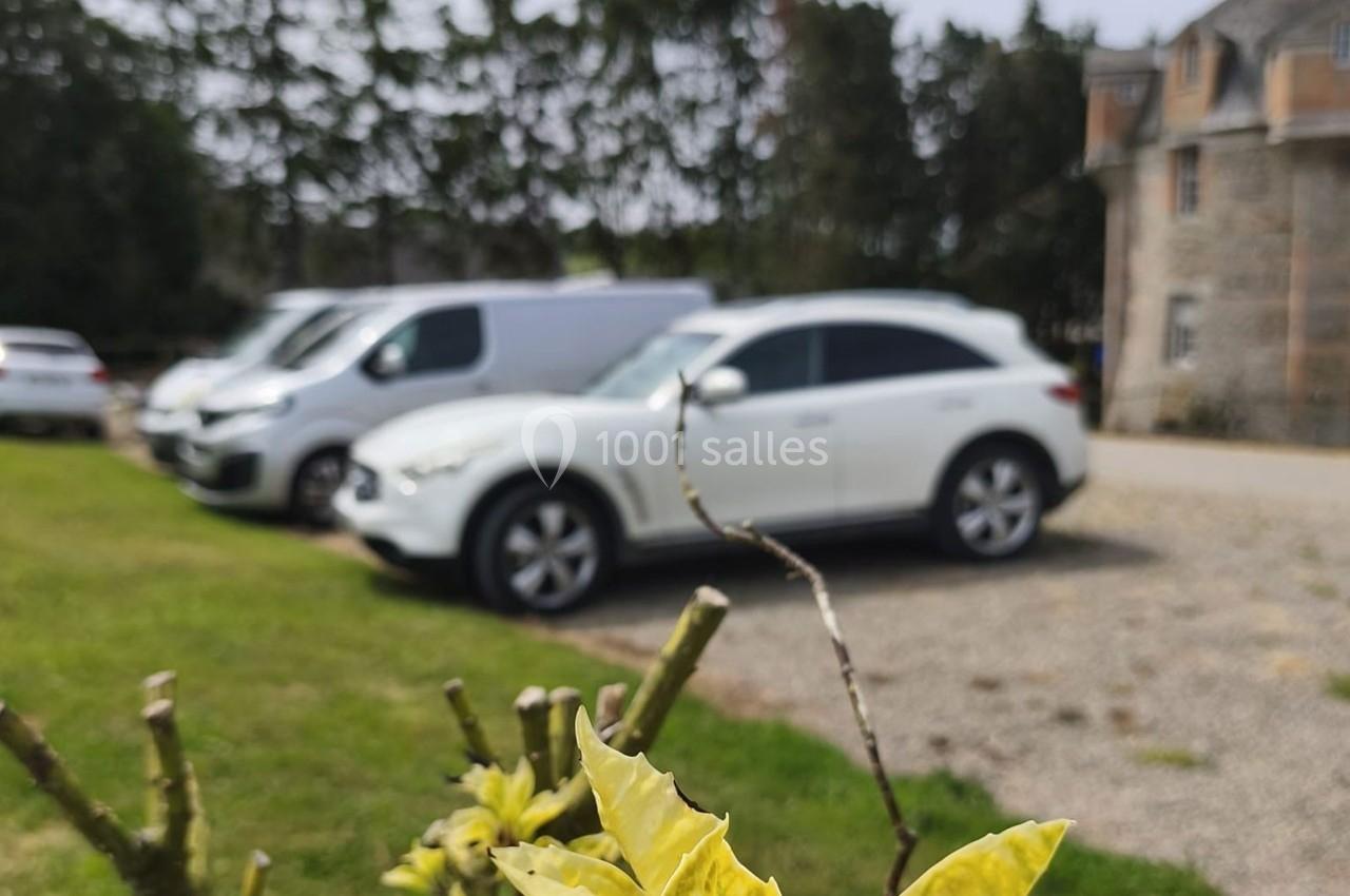 Voitures blanches stationnées sur un parking gravillonné devant un bâtiment en pierre, avec des arbres en arrière-plan.