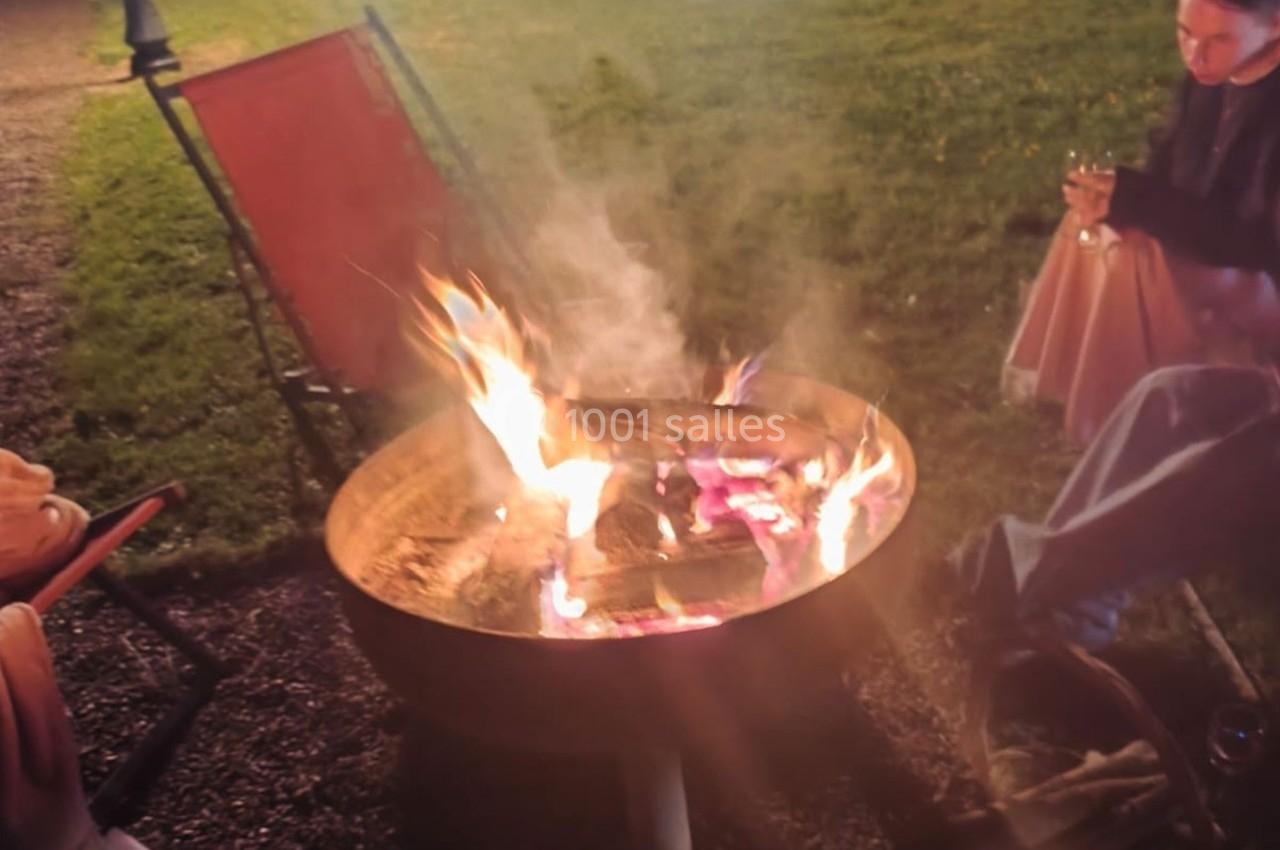 Des personnes assises autour d'un brasero allumé dans un espace extérieur en soirée.