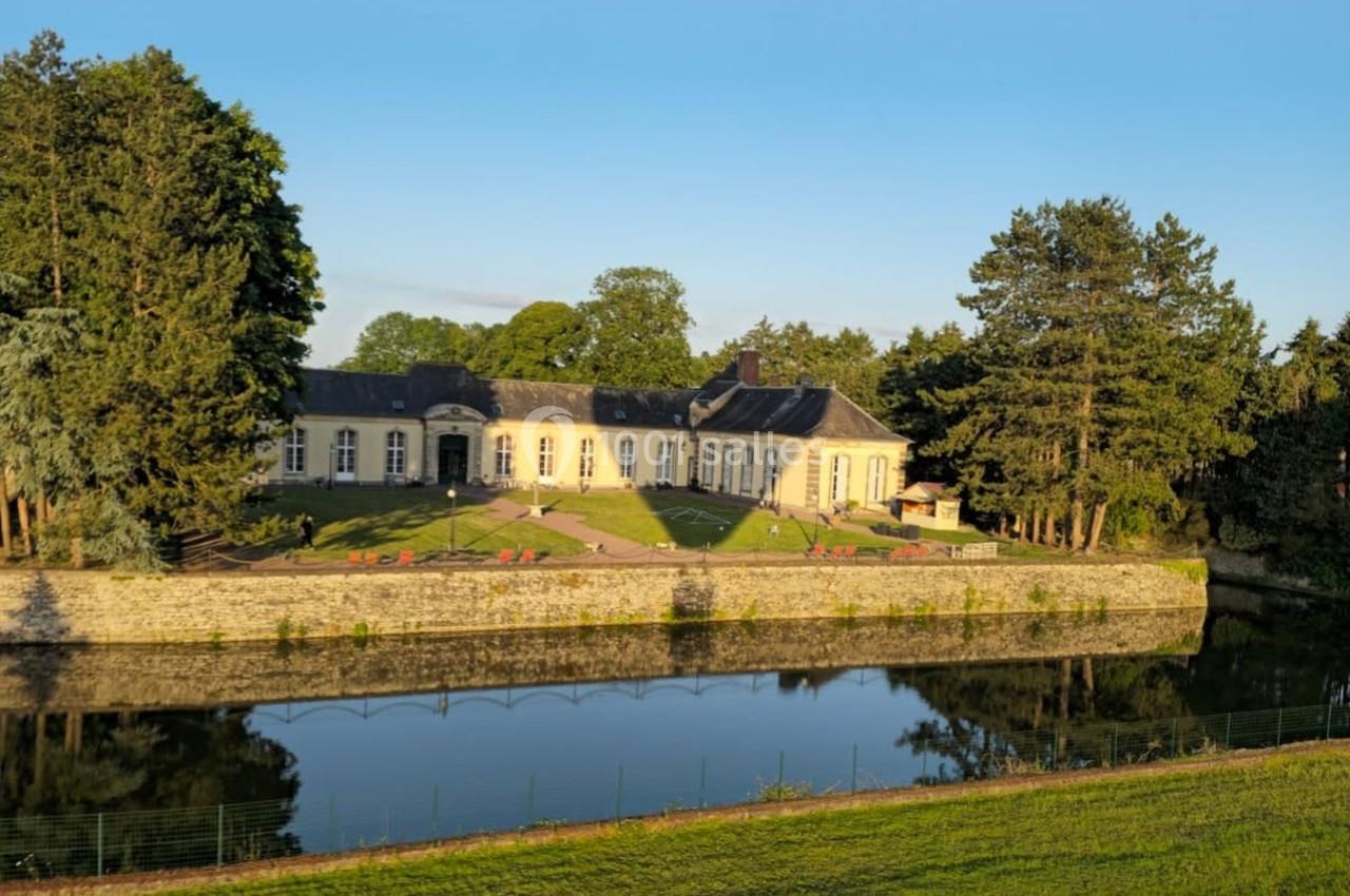 Bâtiment élégant entouré d'arbres, bordant un plan d'eau calme sous un ciel dégagé.