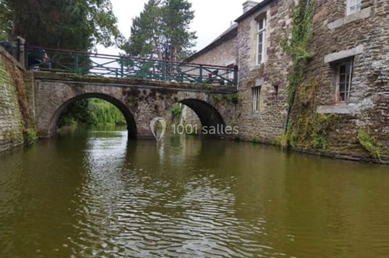 Pont en pierre avec deux arches sur un cours d'eau bordé de bâtiments en pierre et de végétation.