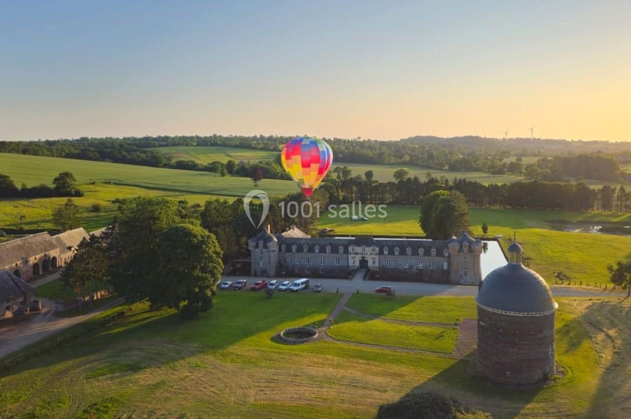Montgolfière colorée survolant un domaine historique entouré de vastes champs verdoyants au coucher du soleil.