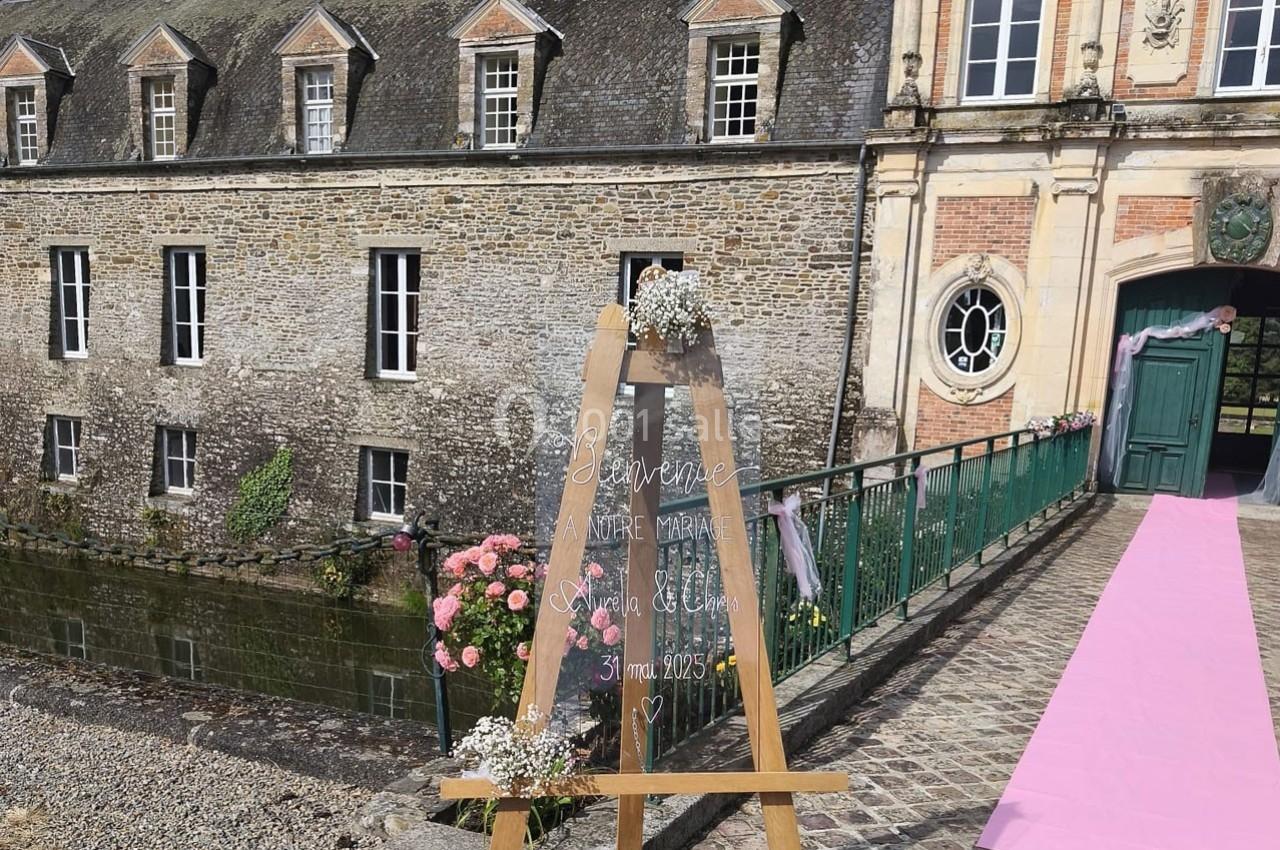Chevalet décoré devant un bâtiment en pierre avec pont et tapis rose menant à une porte ouverte.